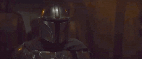 An animated image of a person in a metallic helmet and armor, The Mandalorian, in a dimly lit corridor with walls of rough stone and scattered lights, captioned “This is the way.”