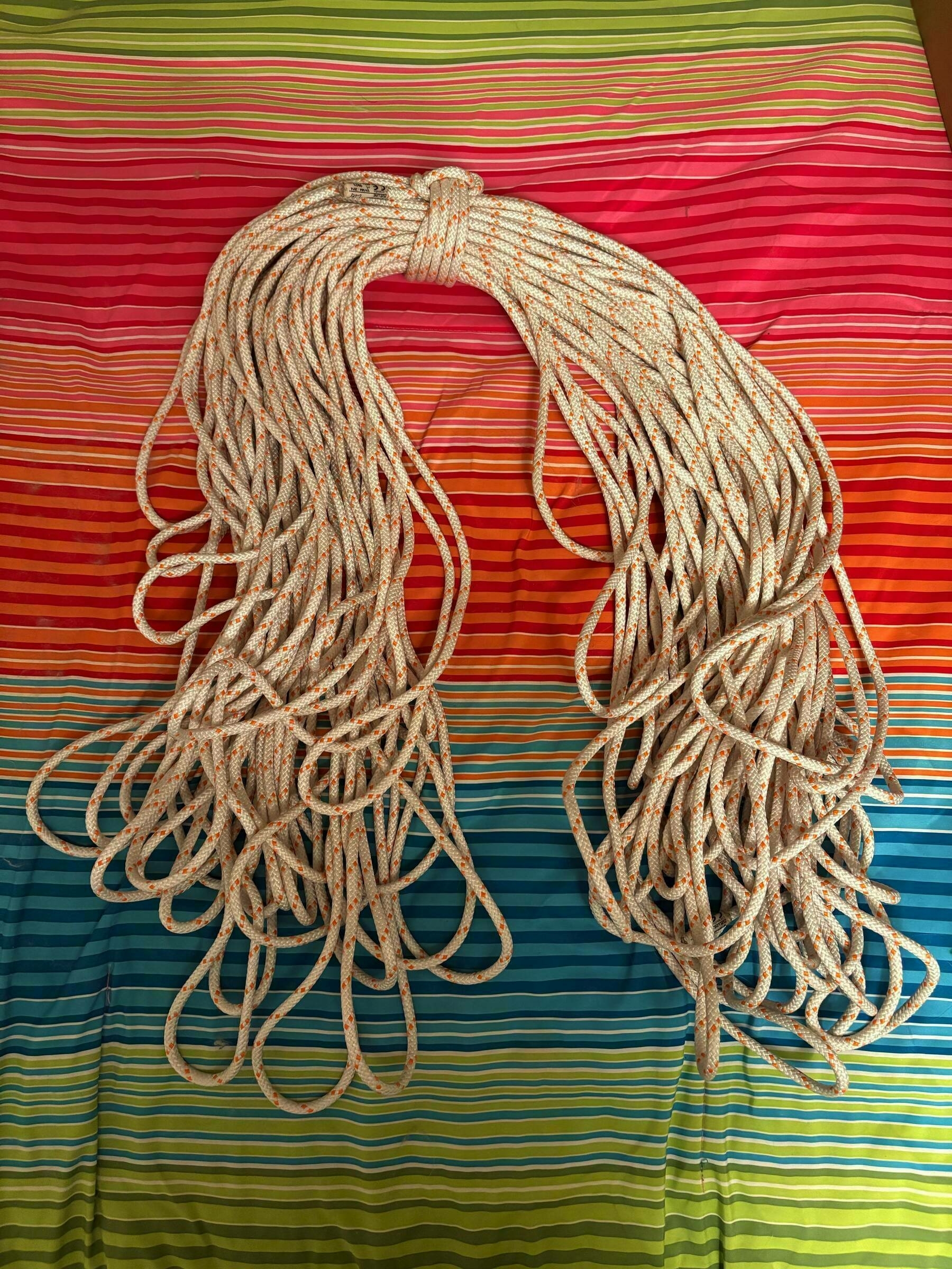 A coiled climbing rope rests neatly on a multi-colored striped bedspread featuring shades of green, red, orange, blue, and yellow.